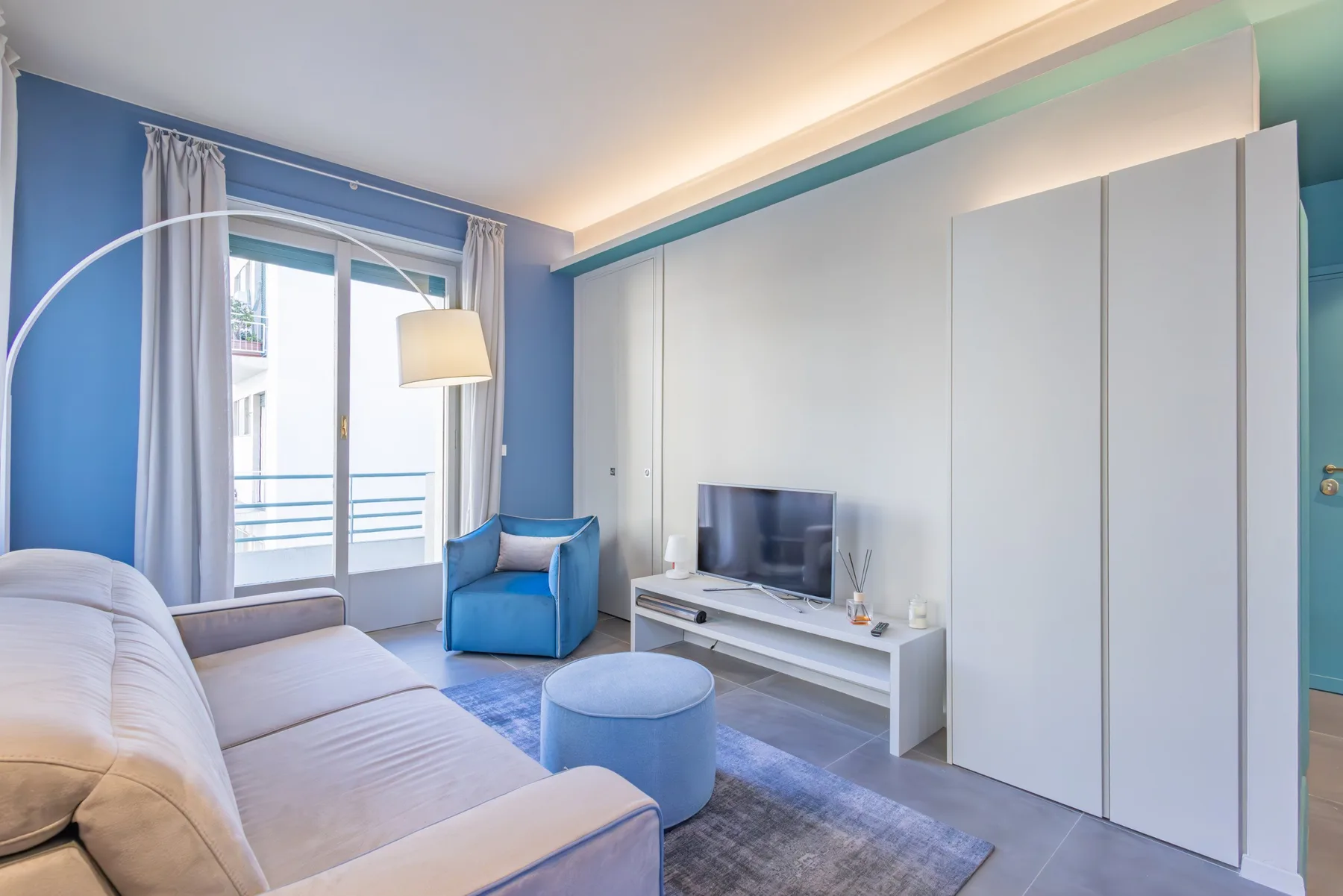 A bright living room with a sofa, blue armchair, and television.