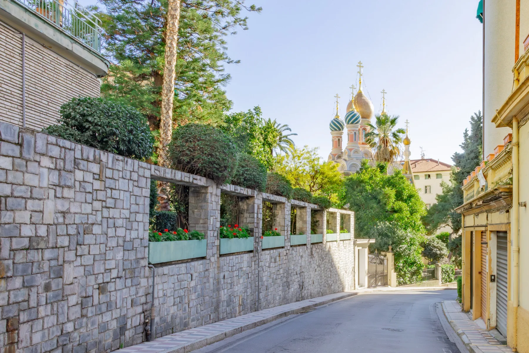 A narrow street passes between stone walls and buildings, with colorful domes in the distance.