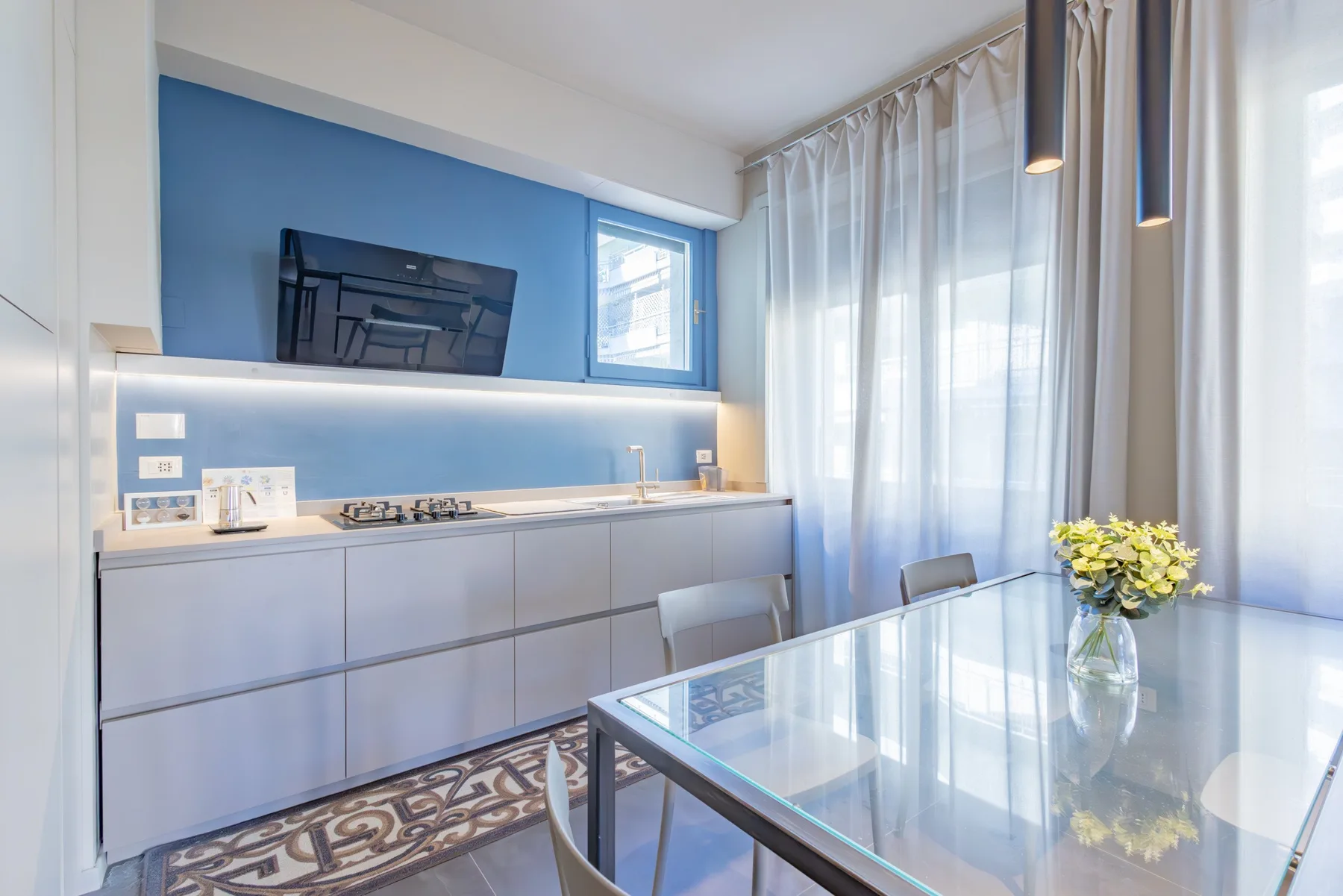 A modern dining area with a glass table beside a compact kitchen.