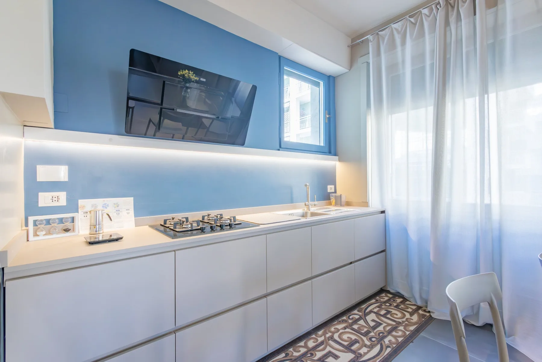 A modern kitchen with a long counter, cooktop, and blue accent wall.