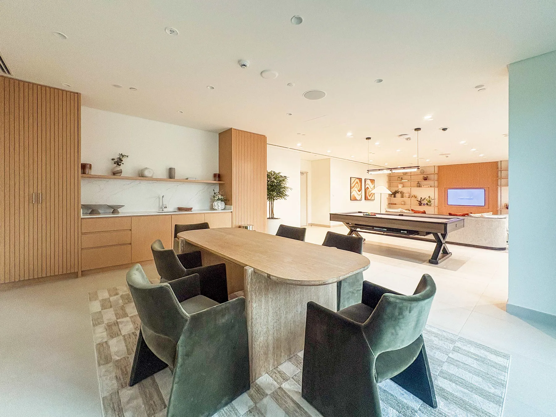A modern dining and living area features a long table with upholstered seating and a billiards table.