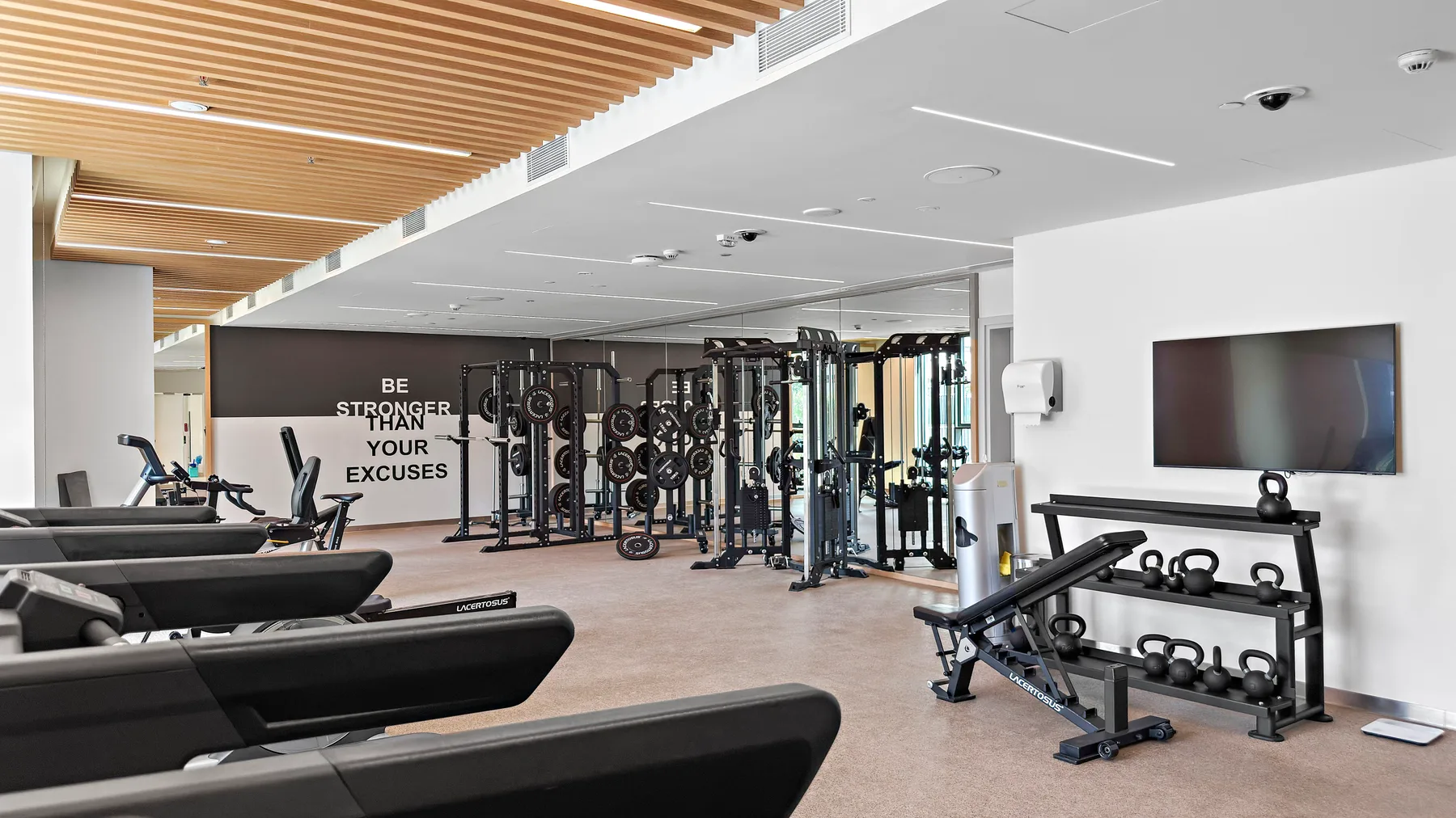 A gym with weight machines, free weights, and a wall-mounted screen.