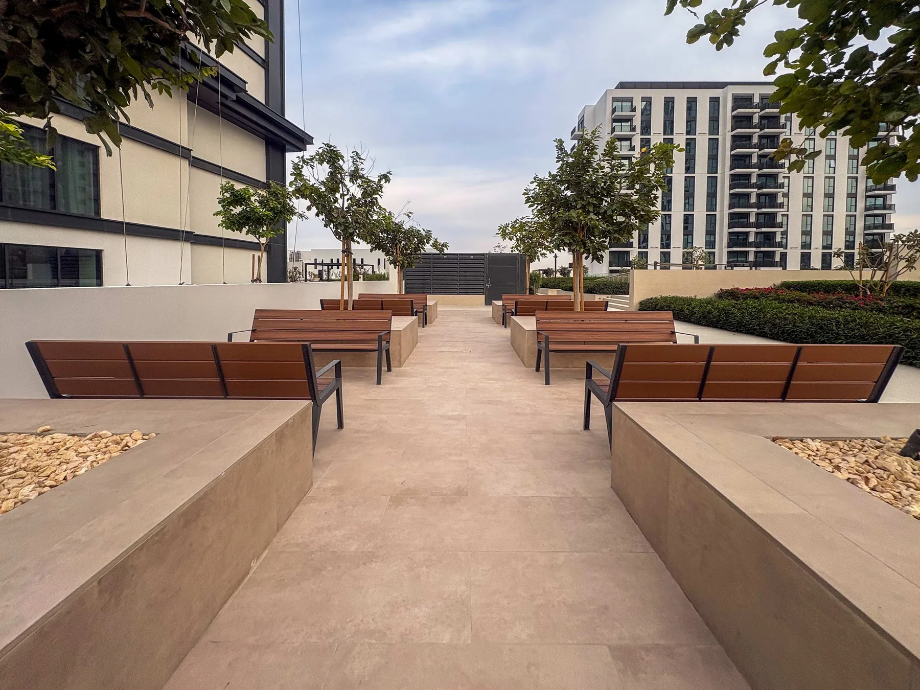 An outdoor seating area has rows of benches along a paved walkway.