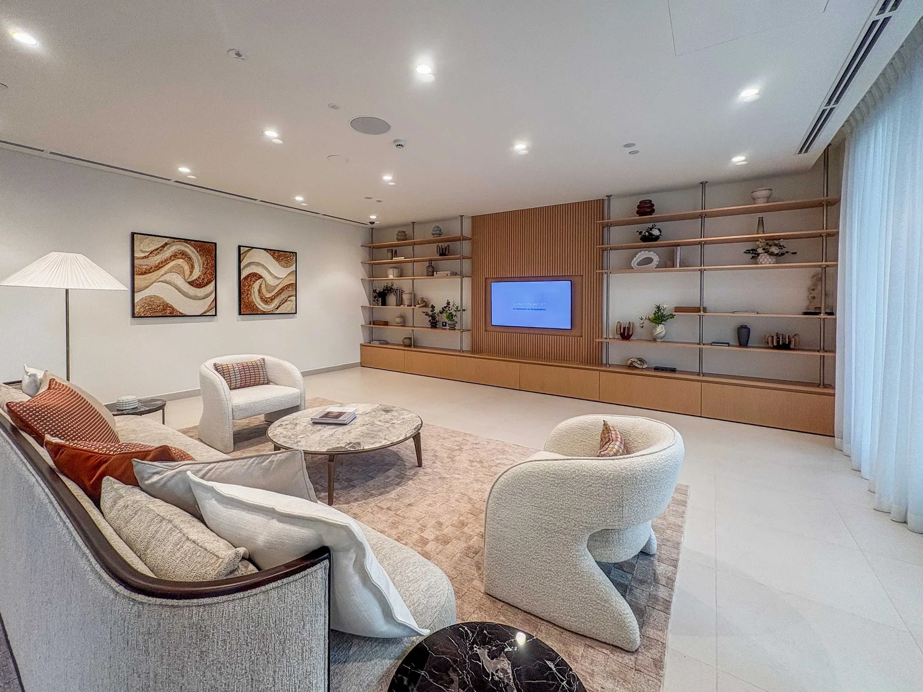 A spacious living room with curved seating, a low table, and built-in display shelves.