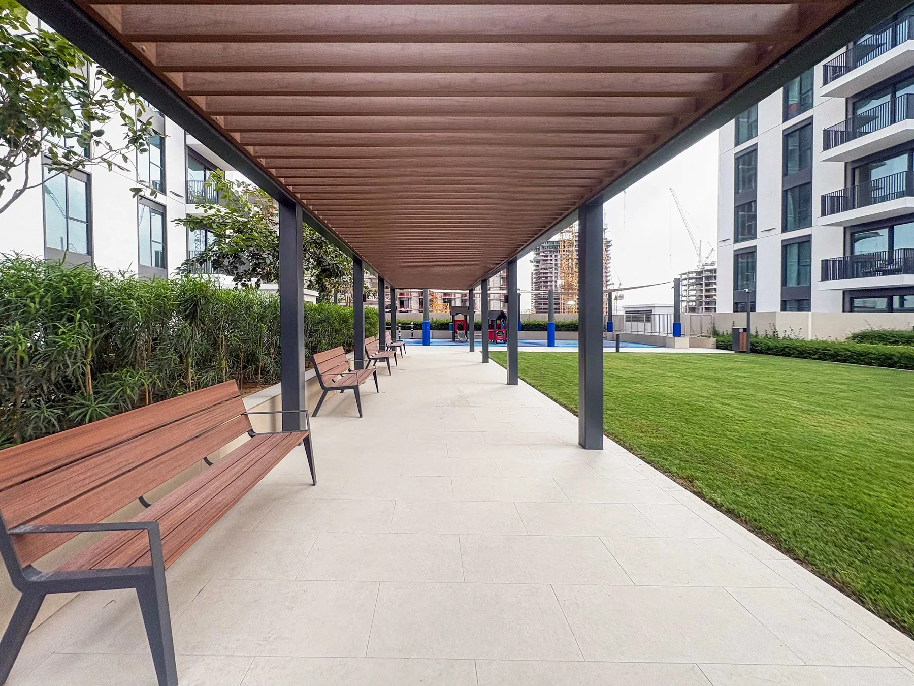 A covered outdoor walkway with seating runs beside a landscaped lawn.