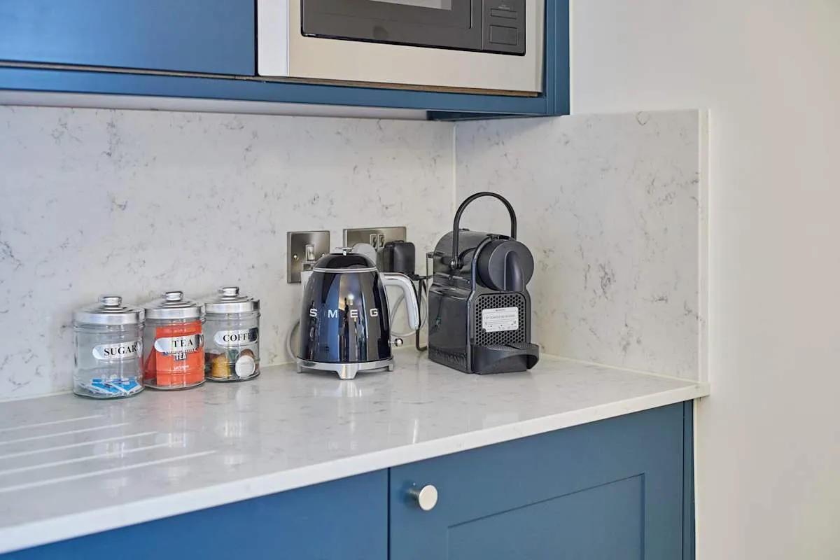 Una encimera de cocina con un hervidor, una cafetera y tres recipientes.