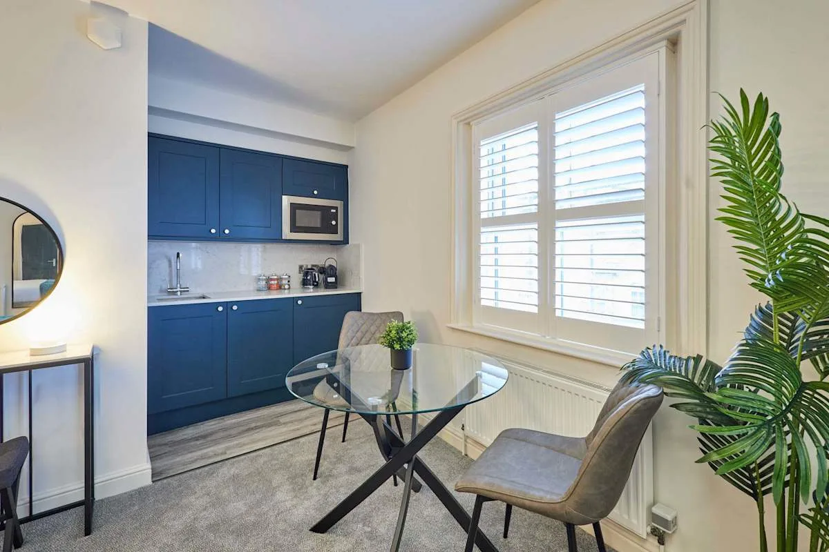 Comedor con una mesa de vidrio junto a una cocina compacta y una ventana luminosa.