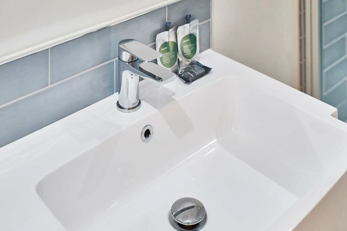 Un lavabo de baño con un grifo cromado y artículos de aseo sobre la encimera.