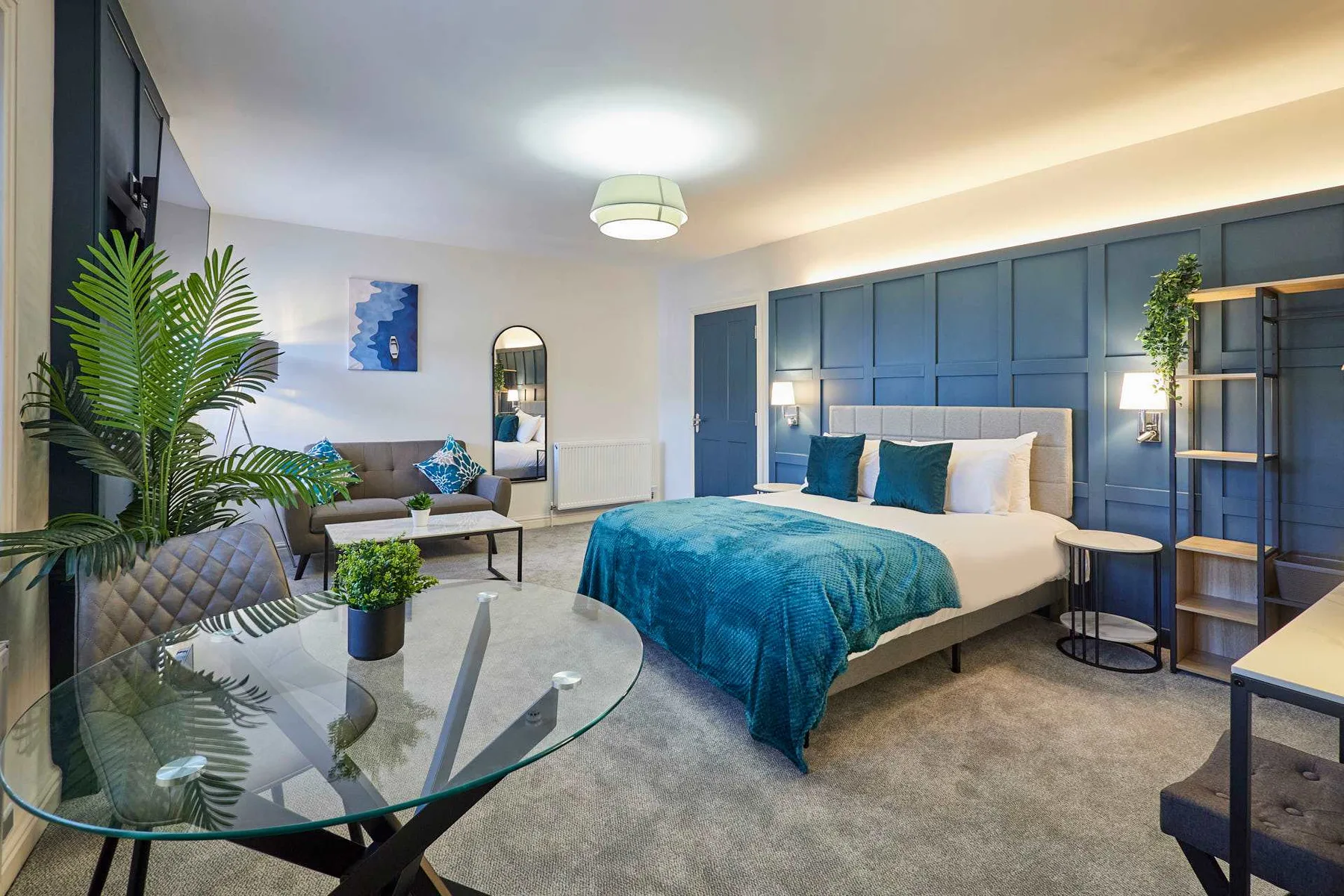Un dormitorio con una cama grande, ropa de cama azul y una mesa de centro de vidrio.