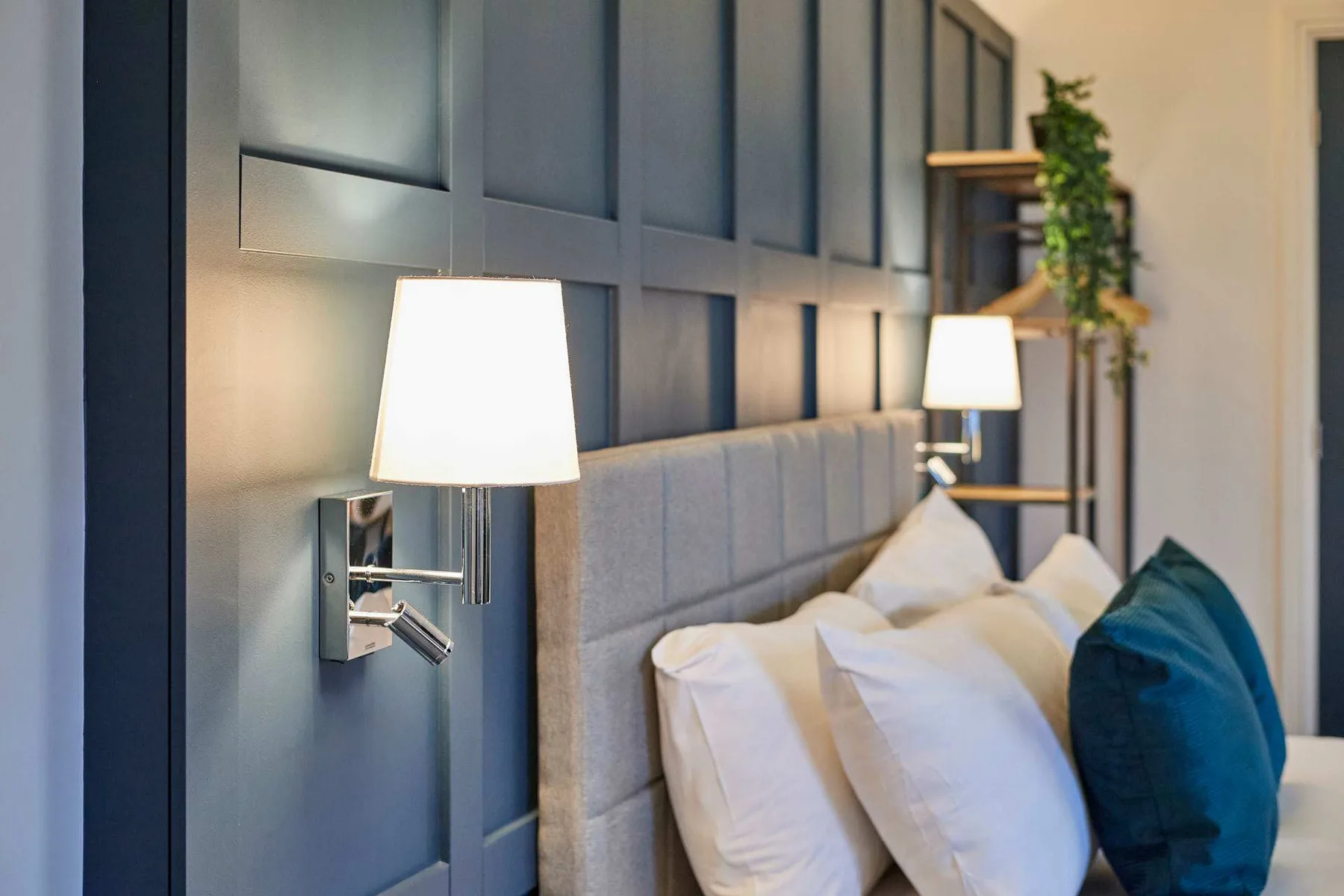 Un dormitorio con una cama bien tendida, lámparas de pared y una pared azul oscuro con paneles.