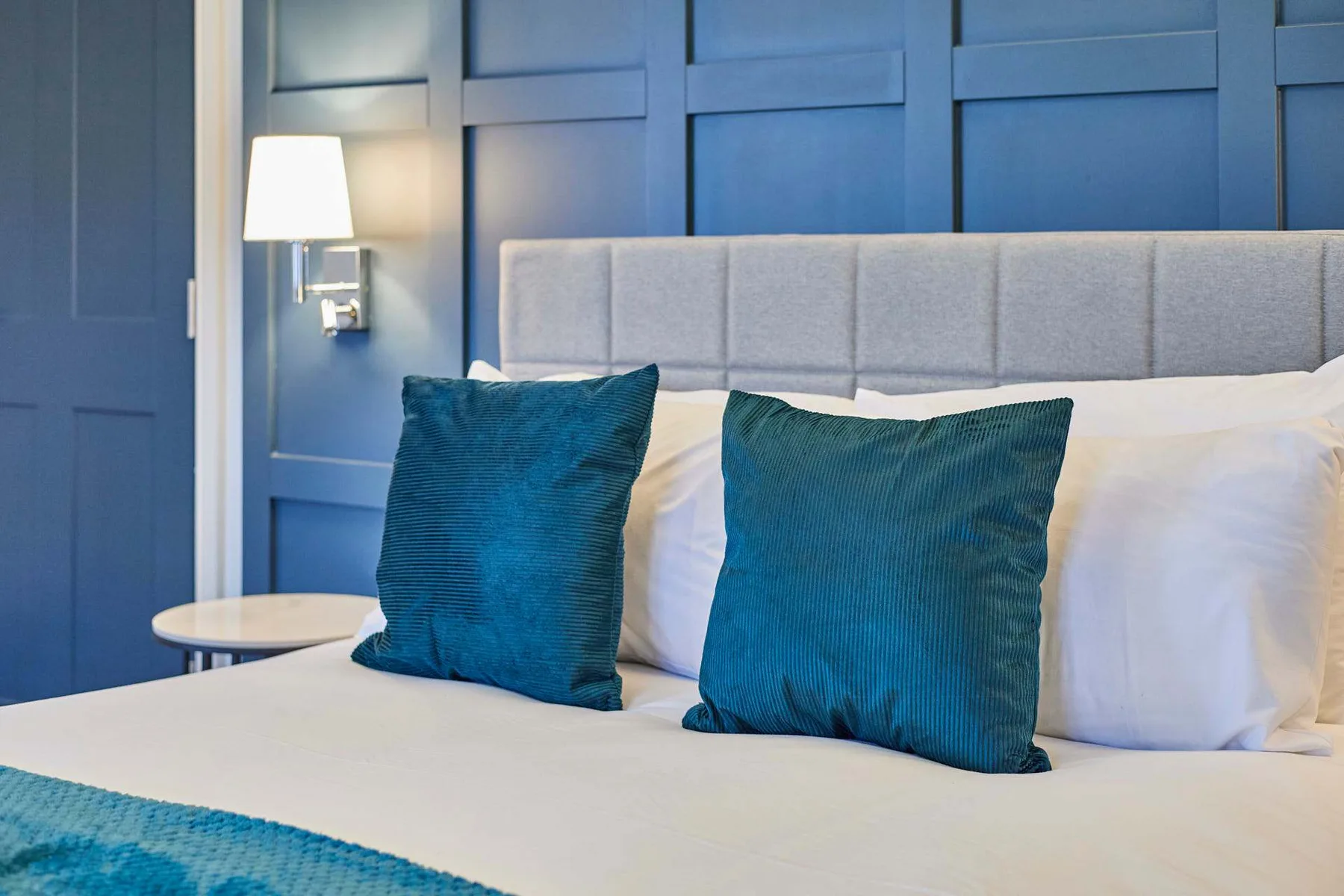 Un dormitorio con una cama, cojines azules y paredes con paneles azules.