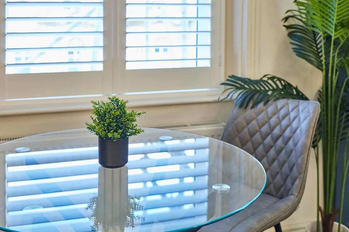Una mesa de comedor de vidrio y asientos acolchados junto a ventanas luminosas.