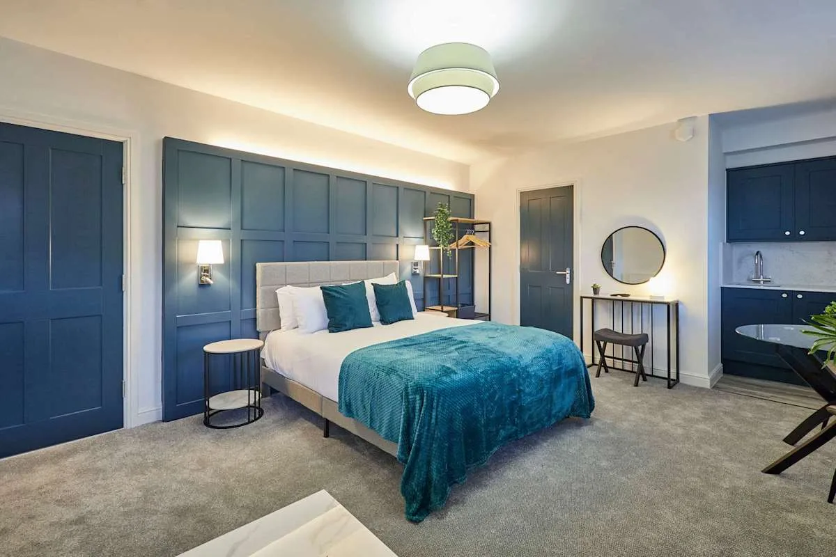Dormitorio con una cama, paneles azul oscuro en la pared y un escritorio pequeño.