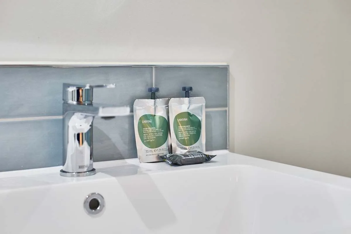 Un lavabo de baño con un grifo cromado y dos sobres de artículos de aseo en el borde.