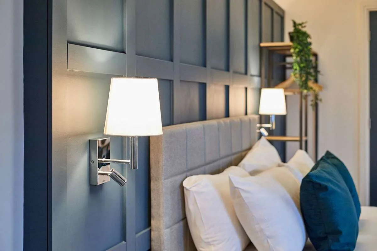 Dormitorio con cabecero acolchado, almohadas blancas y lámparas de pared.