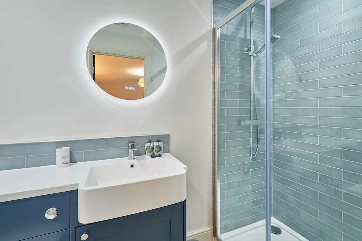 Un baño con lavabo, espejo redondo y ducha con azulejos.