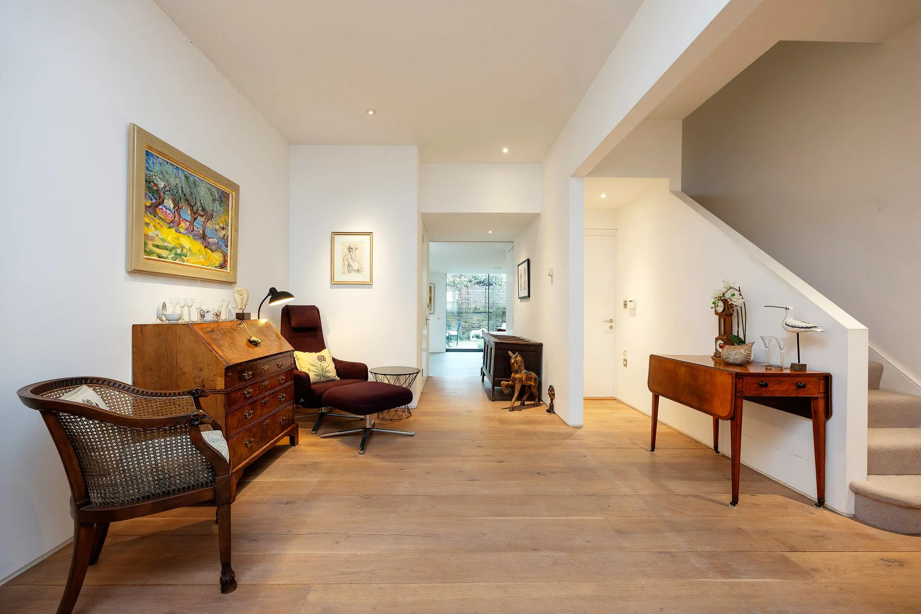 Una sala luminosa con asientos y muebles de madera bajo una escalera.