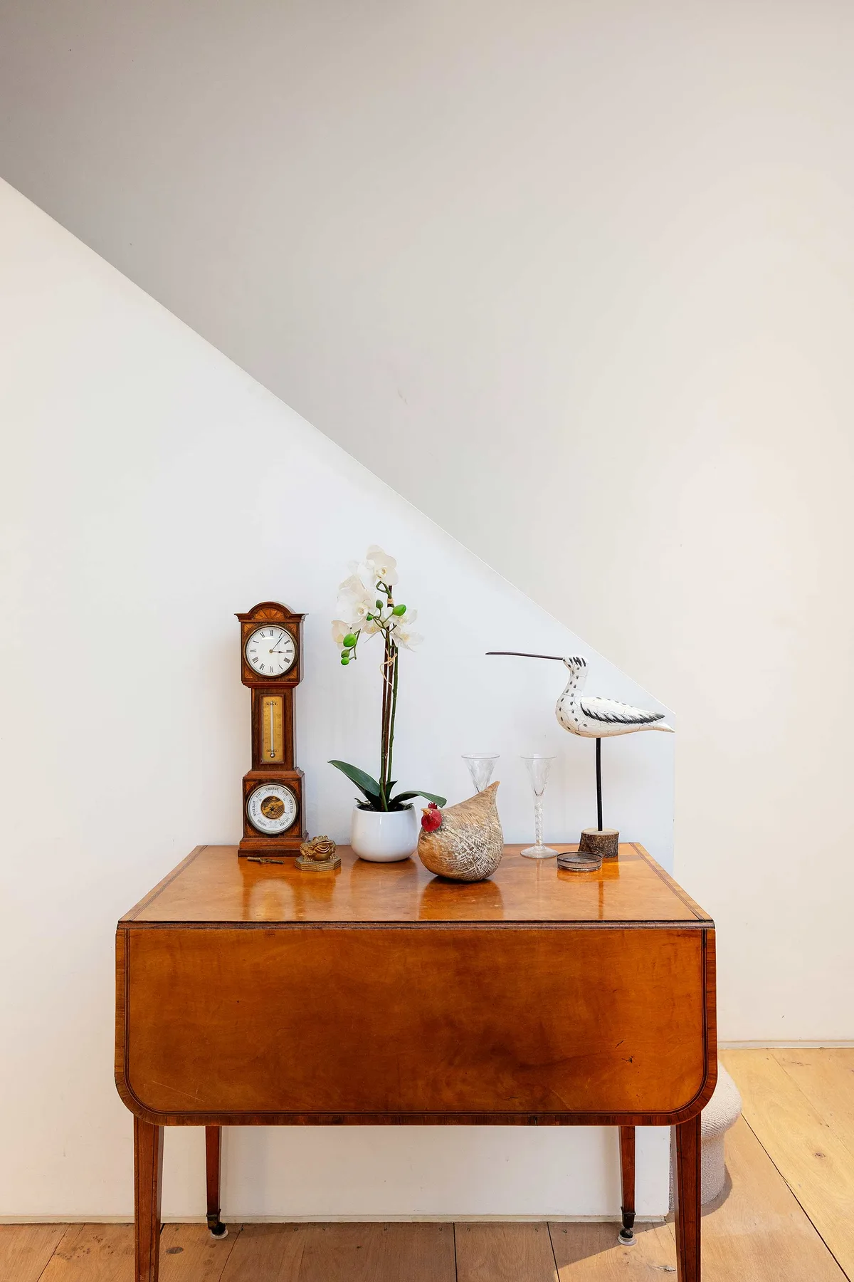 Una consola de madera muestra un reloj, una planta en maceta y objetos decorativos.