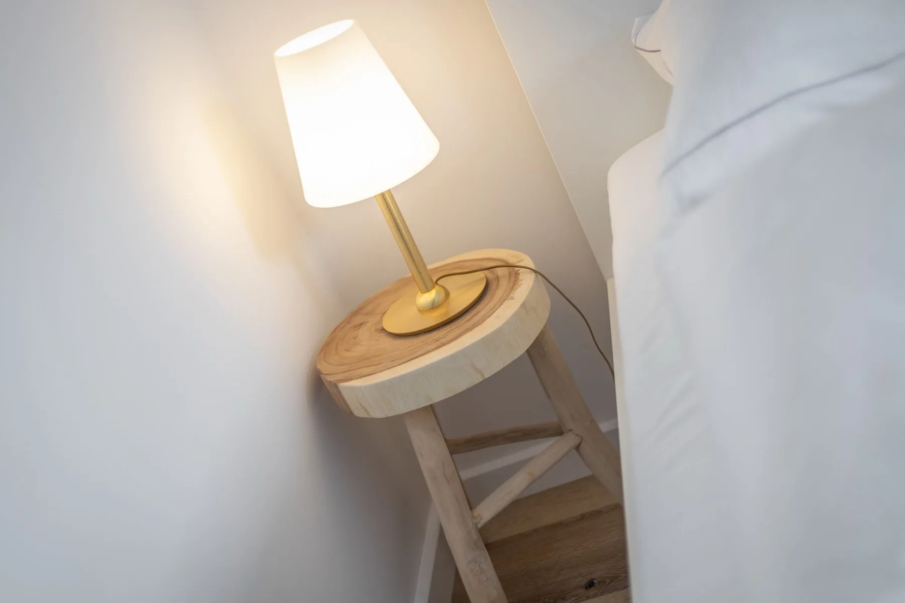 A bedside table with a lit lamp beside a bed.