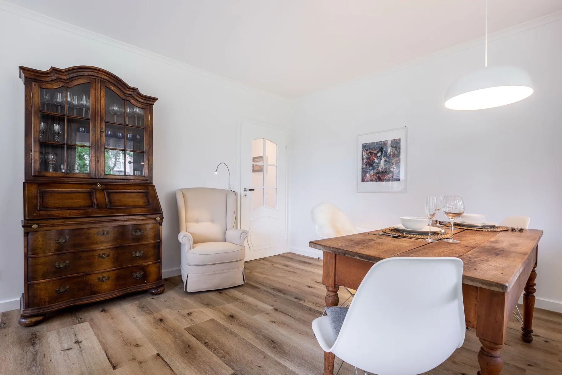 A dining area with a wooden table, white seating, and a glass-front cabinet.