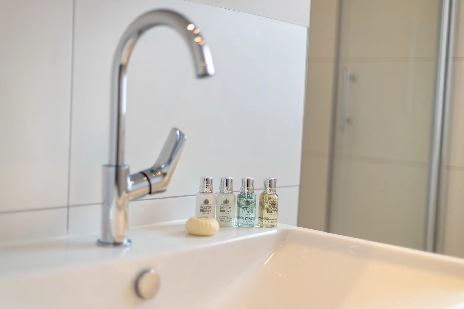A bathroom sink with a curved faucet and small toiletry bottles.
