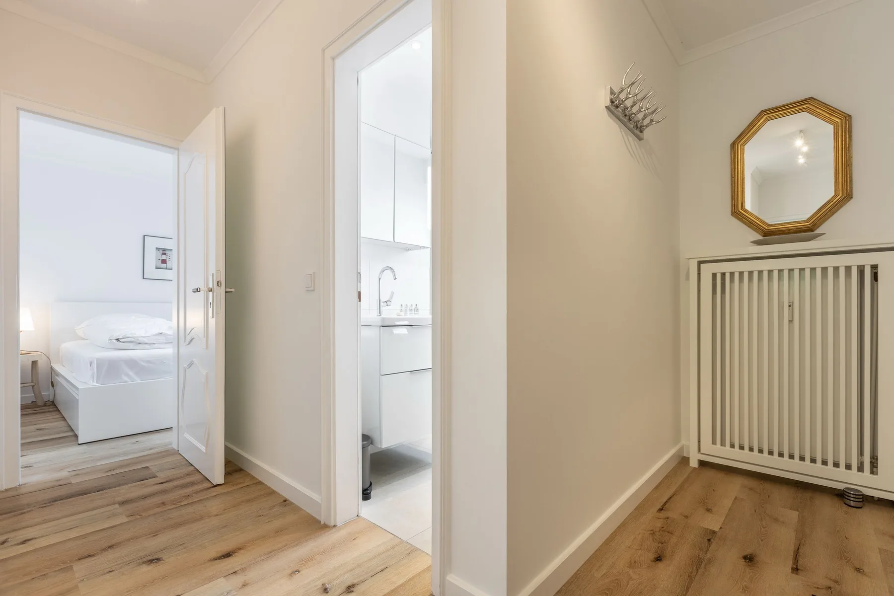 A bright hallway with open doors leading to a bedroom and bathroom.