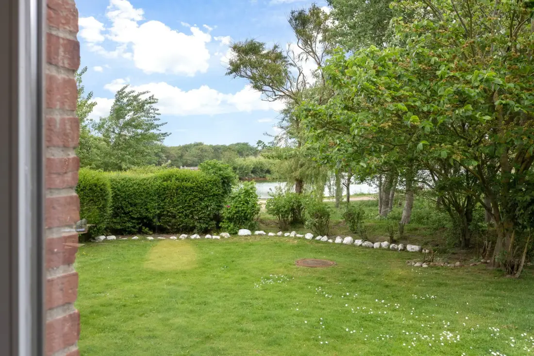 A green garden lawn bordered by hedges and trees, with water visible beyond.
