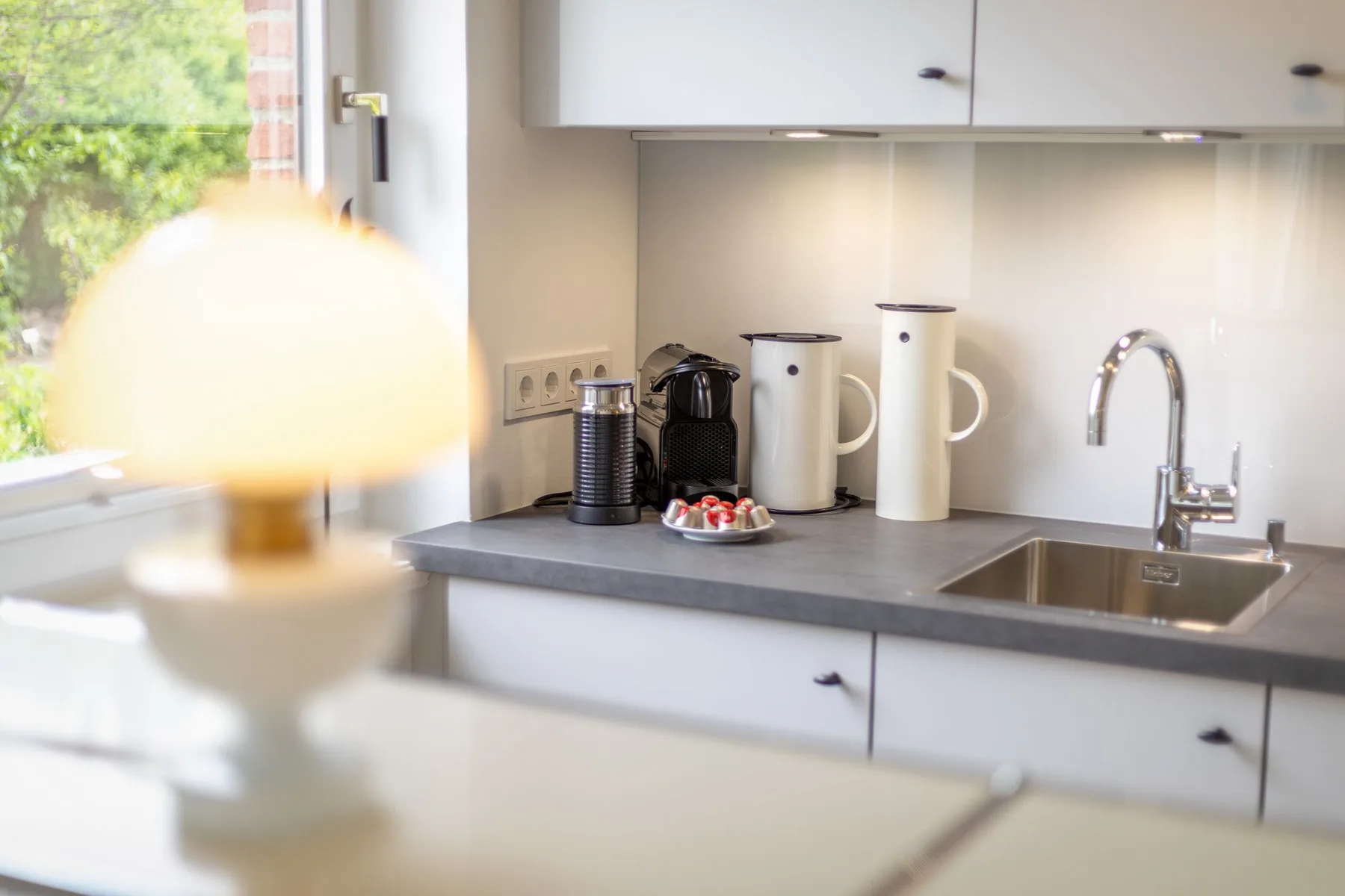 A bright kitchen counter with a sink, coffee maker, and white mugs.
