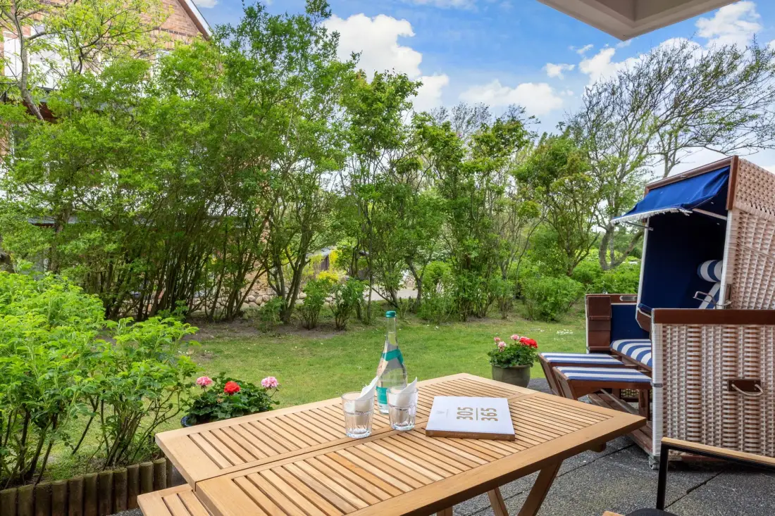 An outdoor patio dining area with a wooden table and garden greenery.