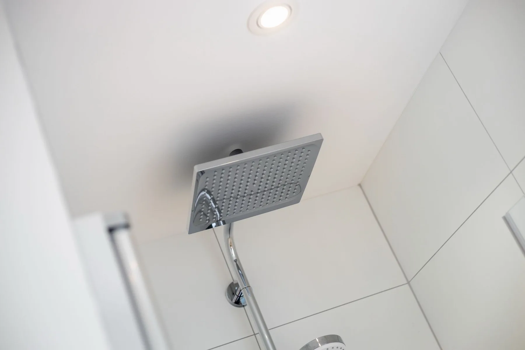A shower with a large overhead showerhead against tiled walls.