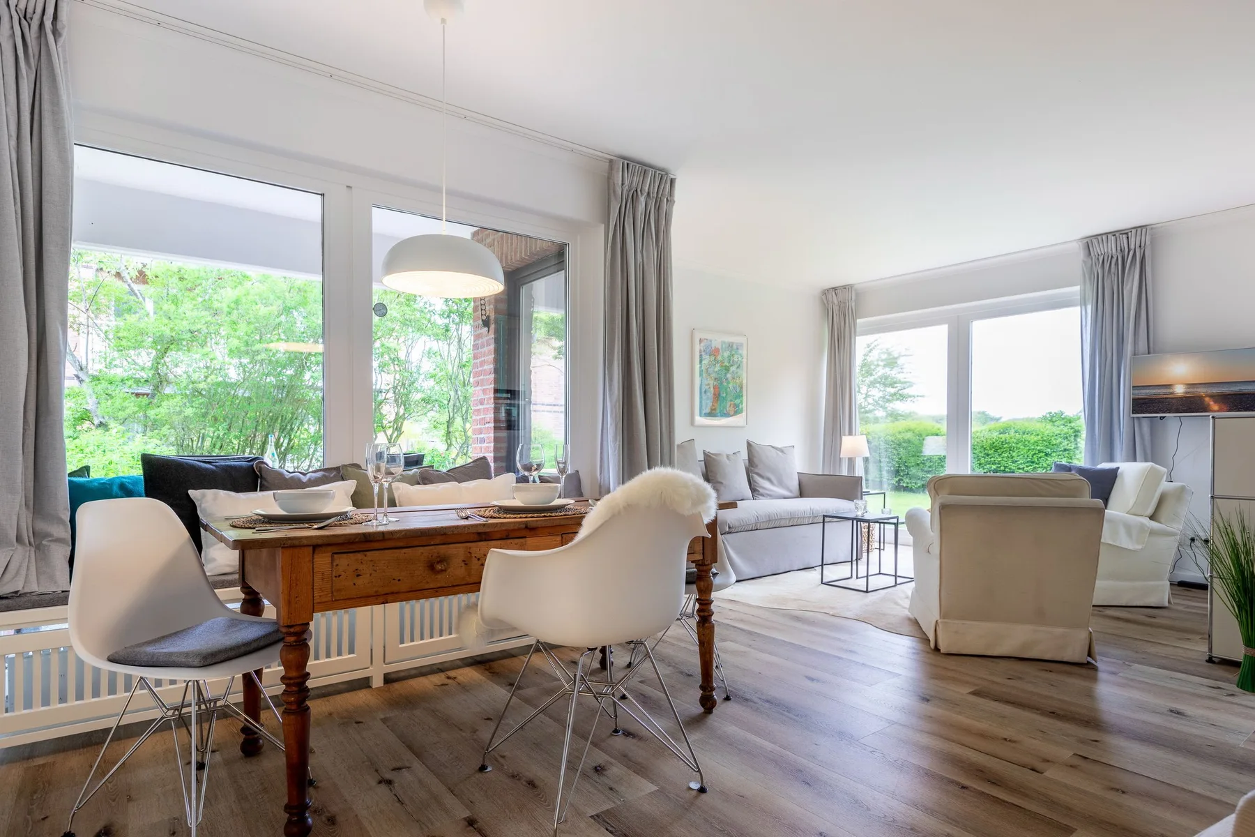 A bright living room with seating around a wooden table and large windows.