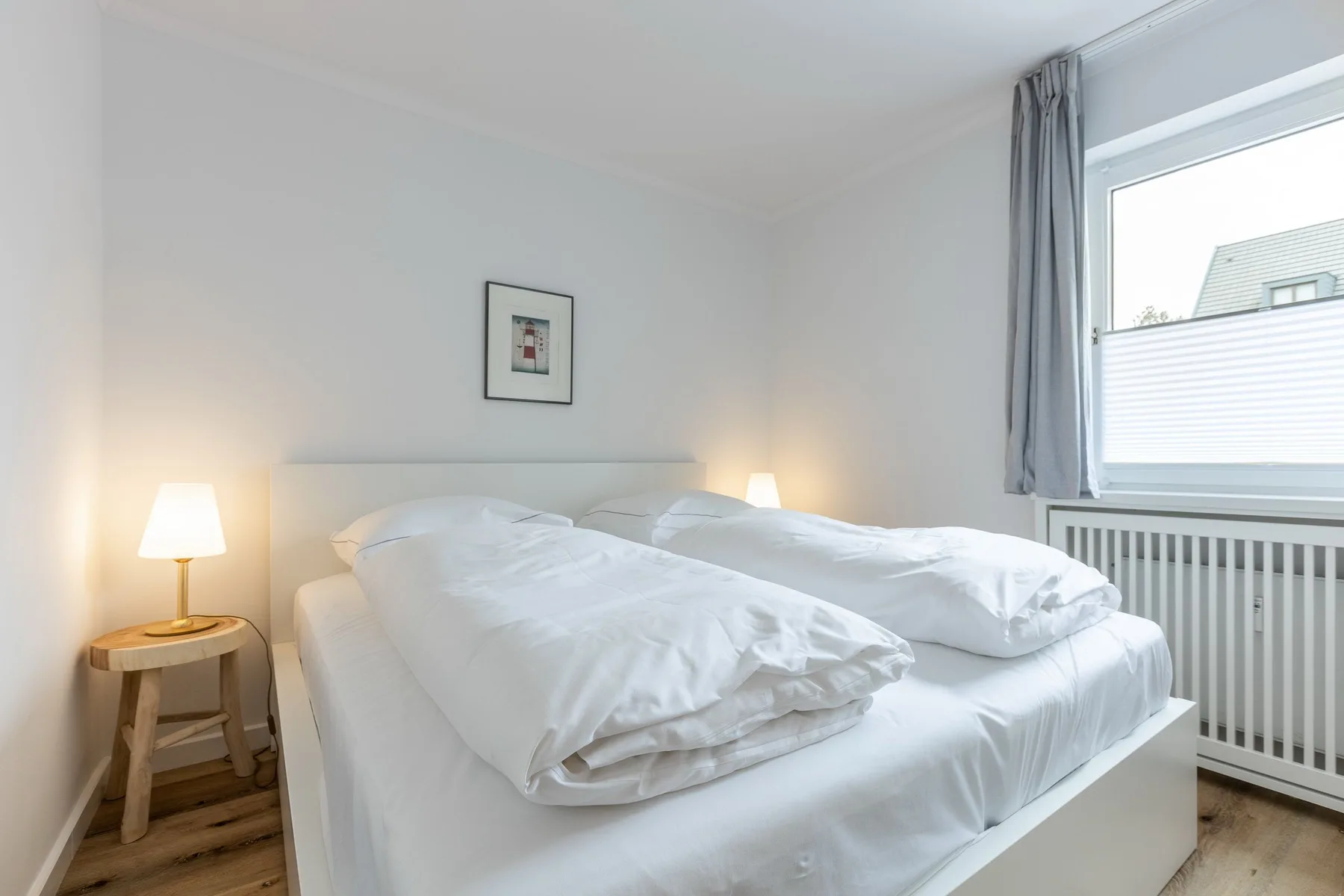 A bright bedroom with a white bed and a window beside it.