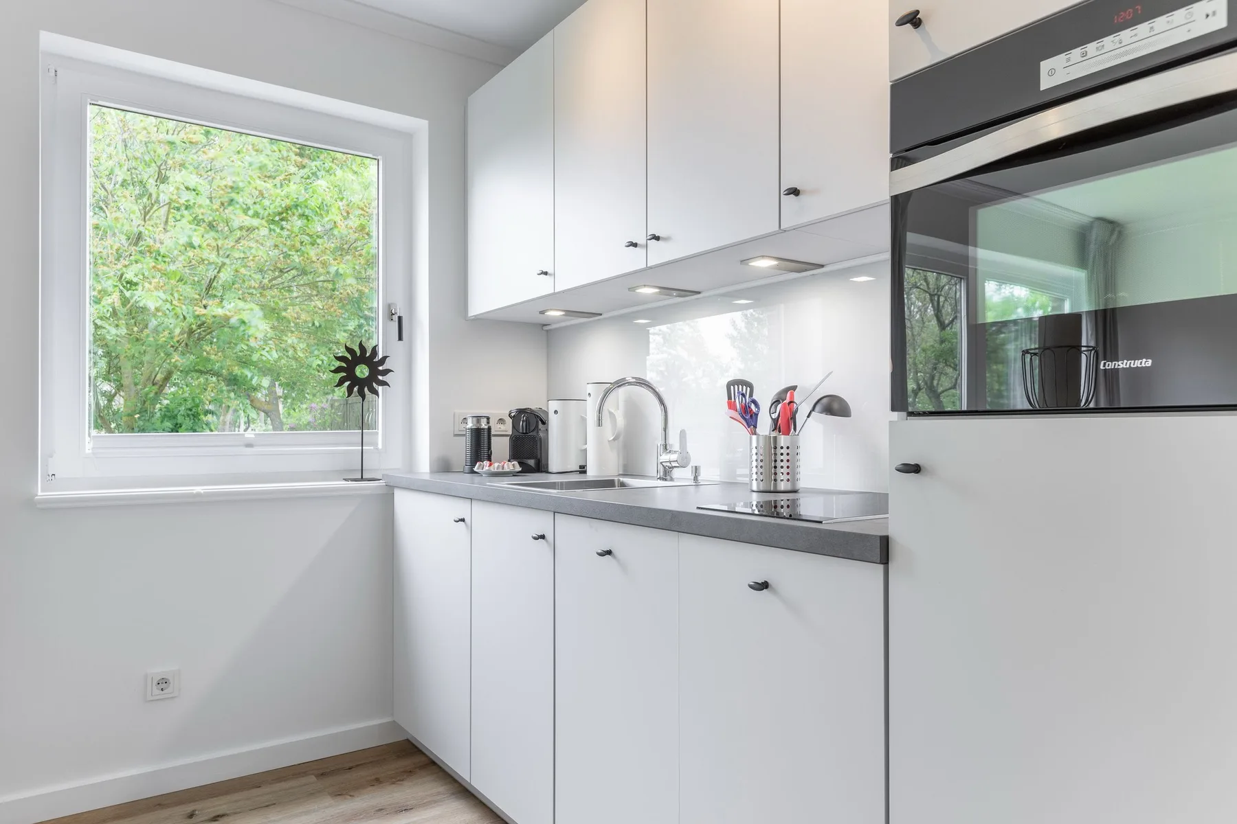 A bright kitchen with white cabinets, a countertop, and a window overlooking greenery.