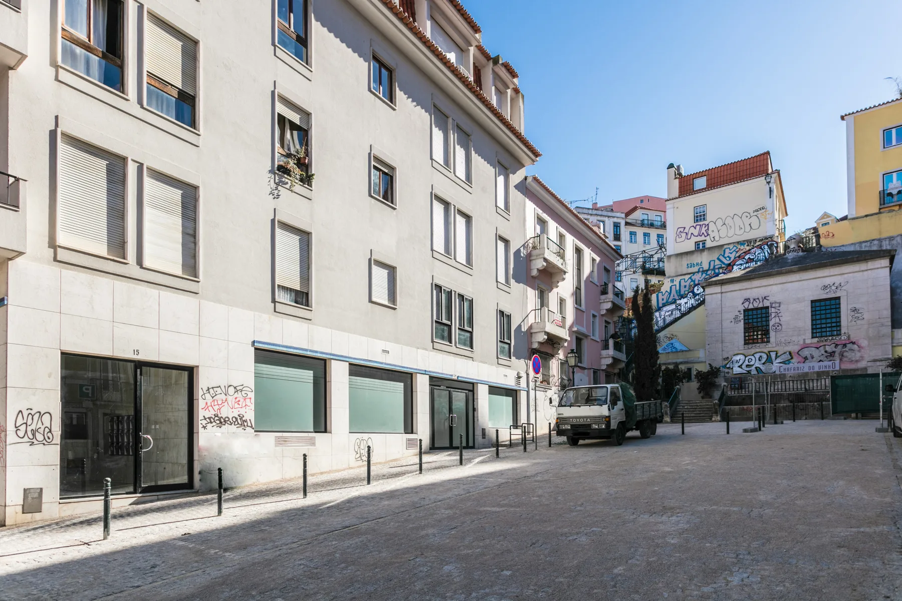 Una calle urbana pavimentada está flanqueada por edificios de apartamentos y locales.