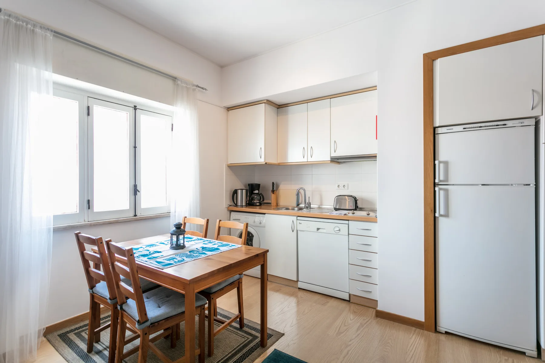 Una cocina luminosa con comedor y una mesa de madera junto a la ventana.