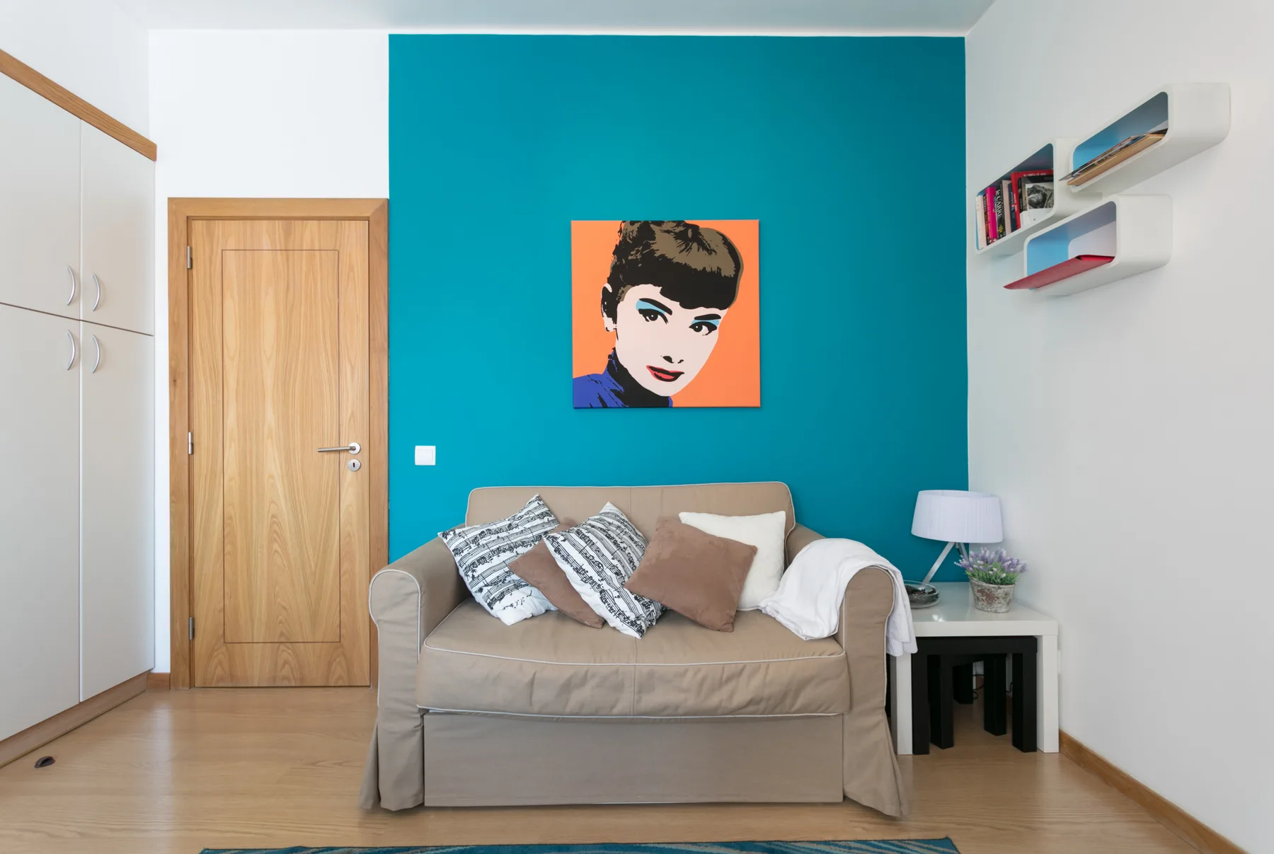 Una sala de estar con un sofá frente a una pared turquesa y un retrato colorido.