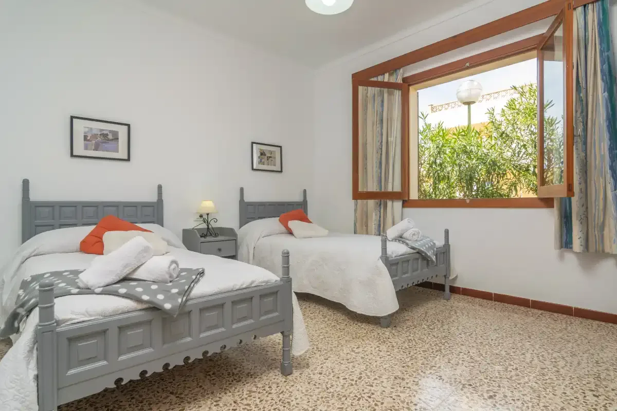 Un dormitorio con dos camas individuales y una ventana abierta con vegetación a la vista.