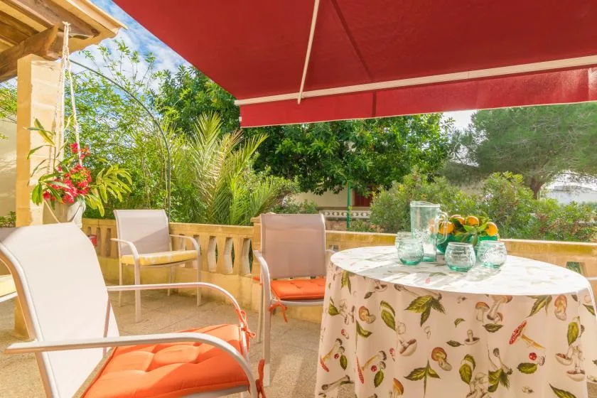 A shaded outdoor patio has seating and a round table set with glassware.