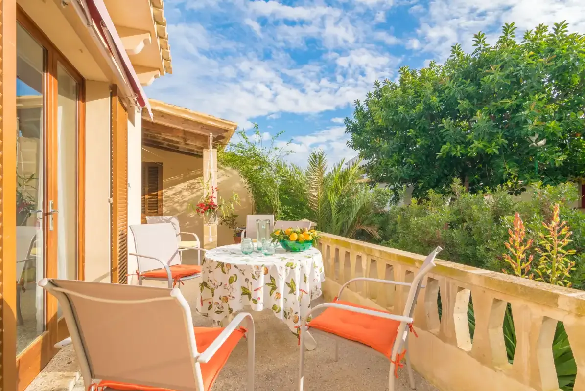 Una terraza al aire libre con una mesa, asientos y abundante vegetación.