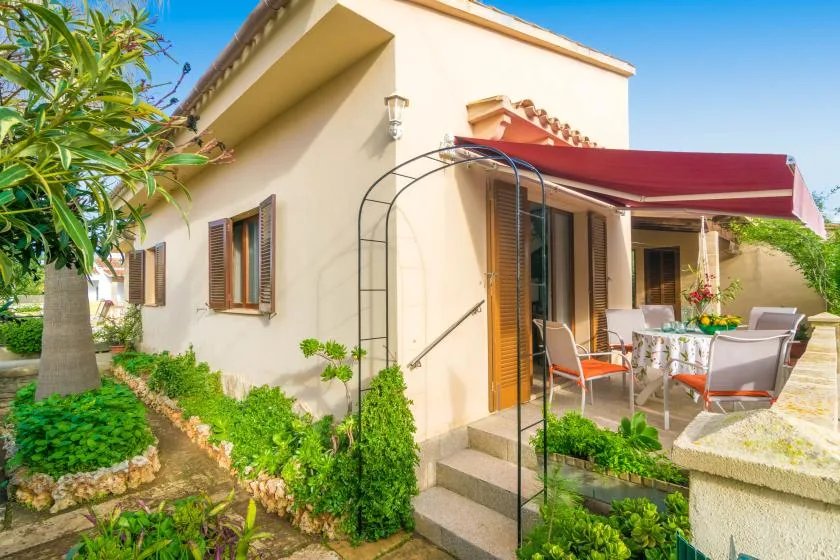 A sunny house patio with outdoor seating beneath a red awning.