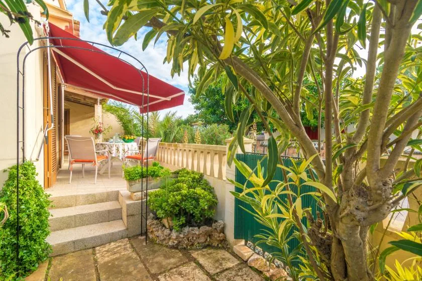 A garden patio with outdoor seating beneath a red awning and leafy trees.