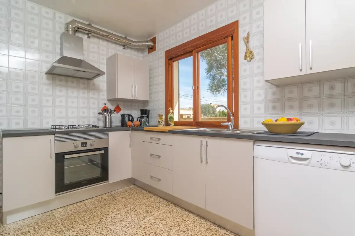 Una cocina con gabinetes claros, una encimera y una ventana con vista a árboles.