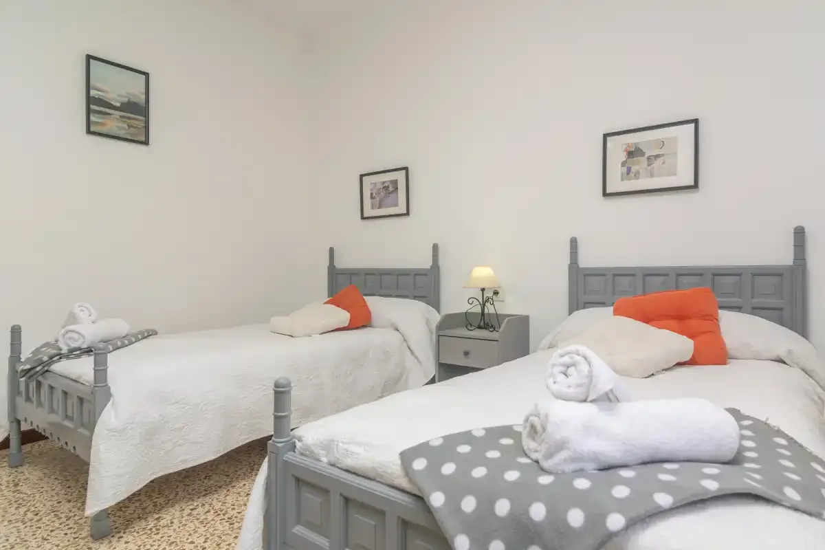 Un dormitorio con dos camas, ropa de cama blanca y cuadros en las paredes.