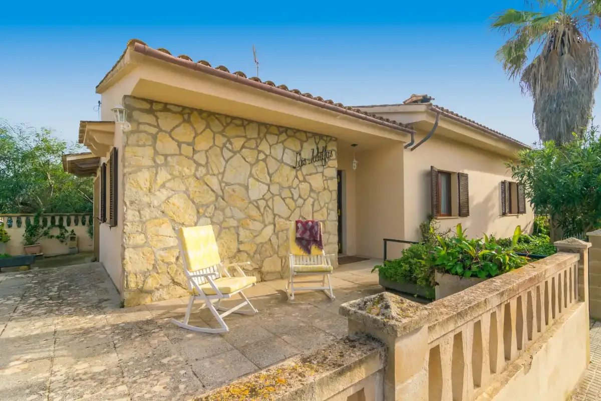 Exterior de una casa de piedra con un pequeño patio y dos sillas reclinables.