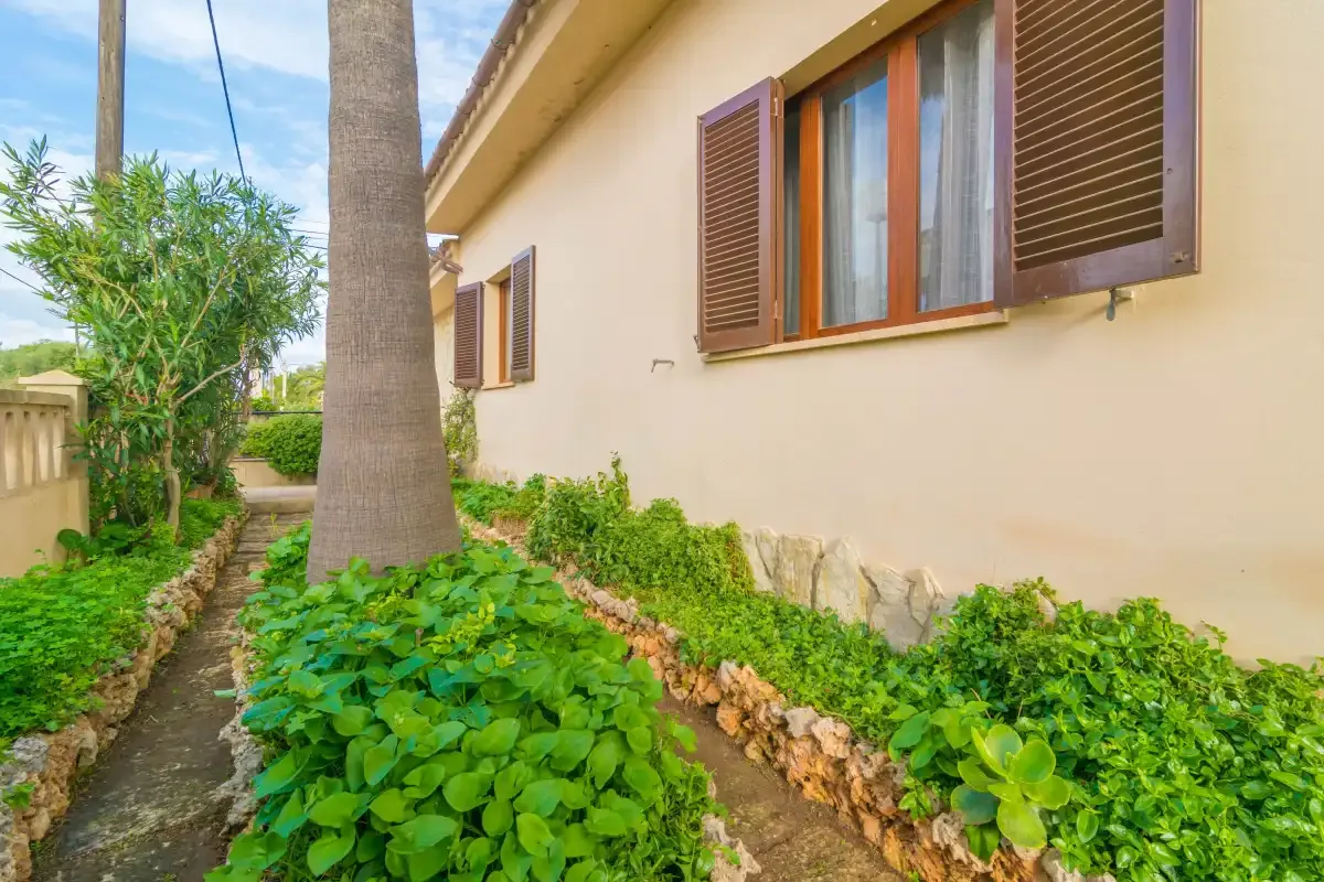 Un sendero de jardín bordea una casa color crema con contraventanas marrones.