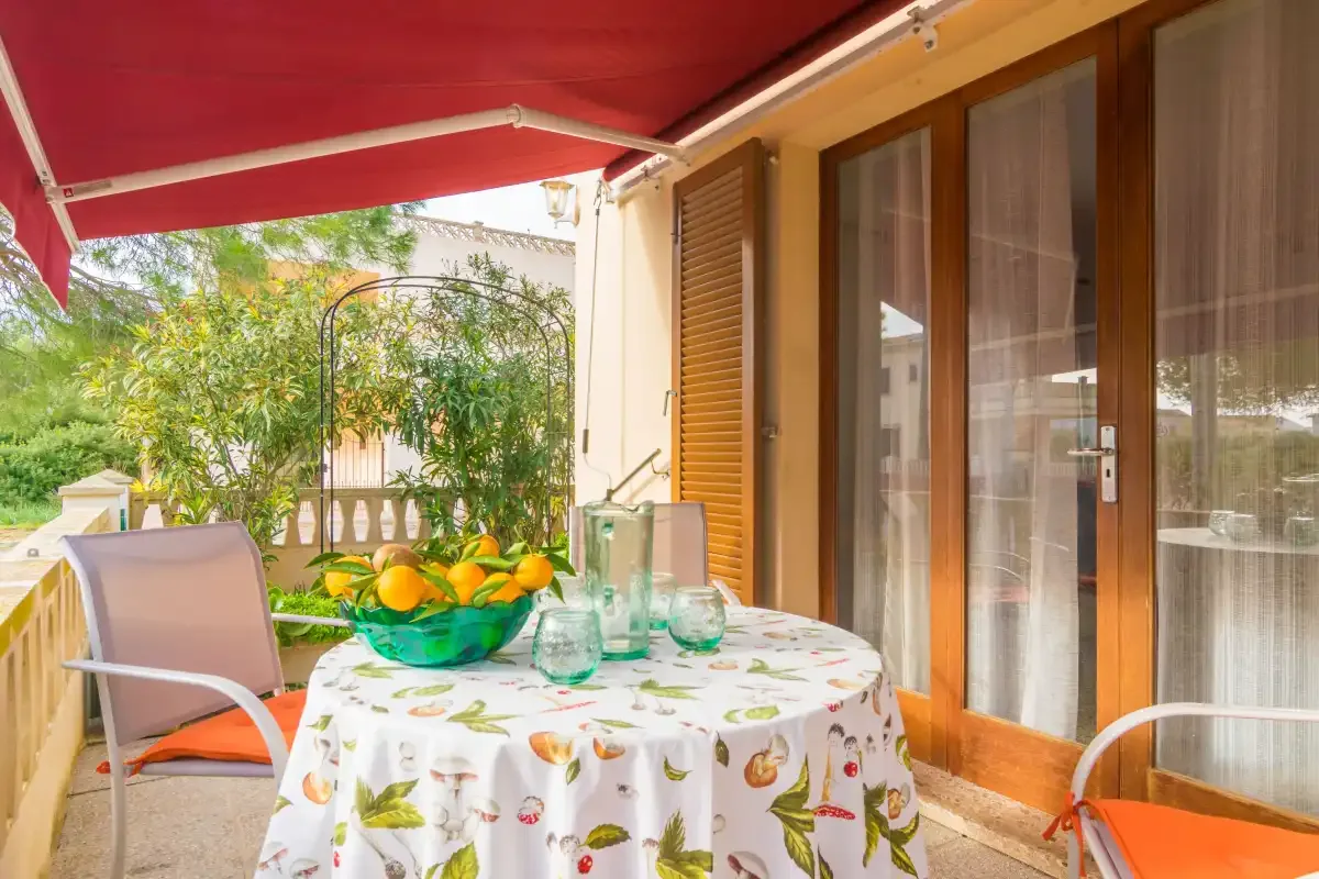 Un patio al aire libre con mesa, asientos y un toldo rojo.
