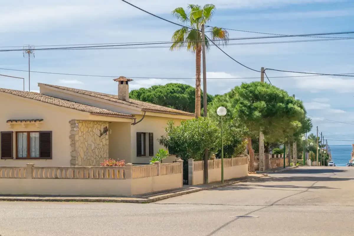 Una casa baja y palmeras bordean una calle tranquila junto al mar.