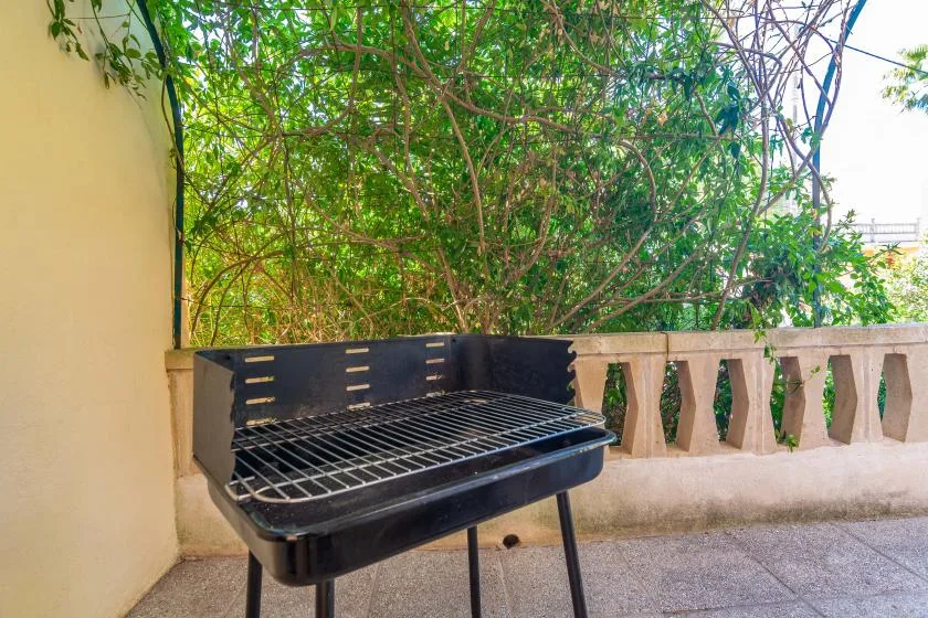 Una terraza exterior con una barbacoa negra junto a una barandilla frondosa.