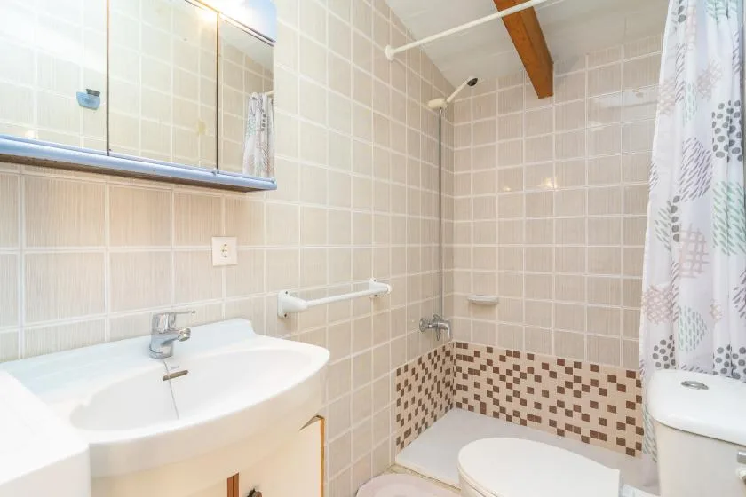 Un baño con azulejos, lavabo, inodoro y una zona de ducha tras una cortina.