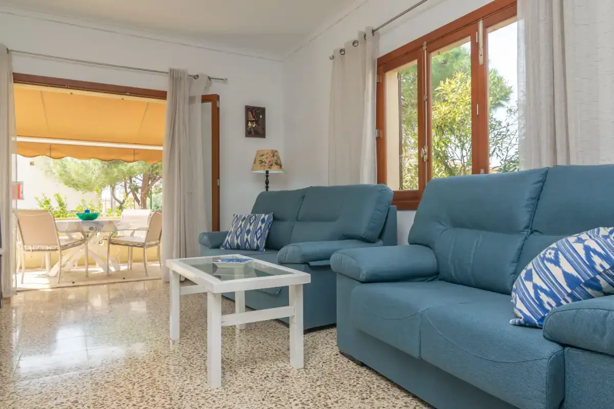 Una sala de estar con asientos azules y una mesa de centro de vidrio junto a un patio soleado.
